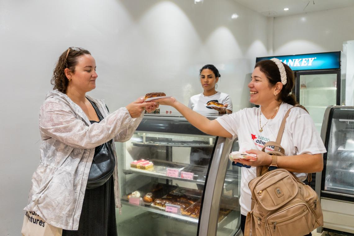 A Cuban Adventures tour guide hands a piece of cake to a tourist in a Havana bakery