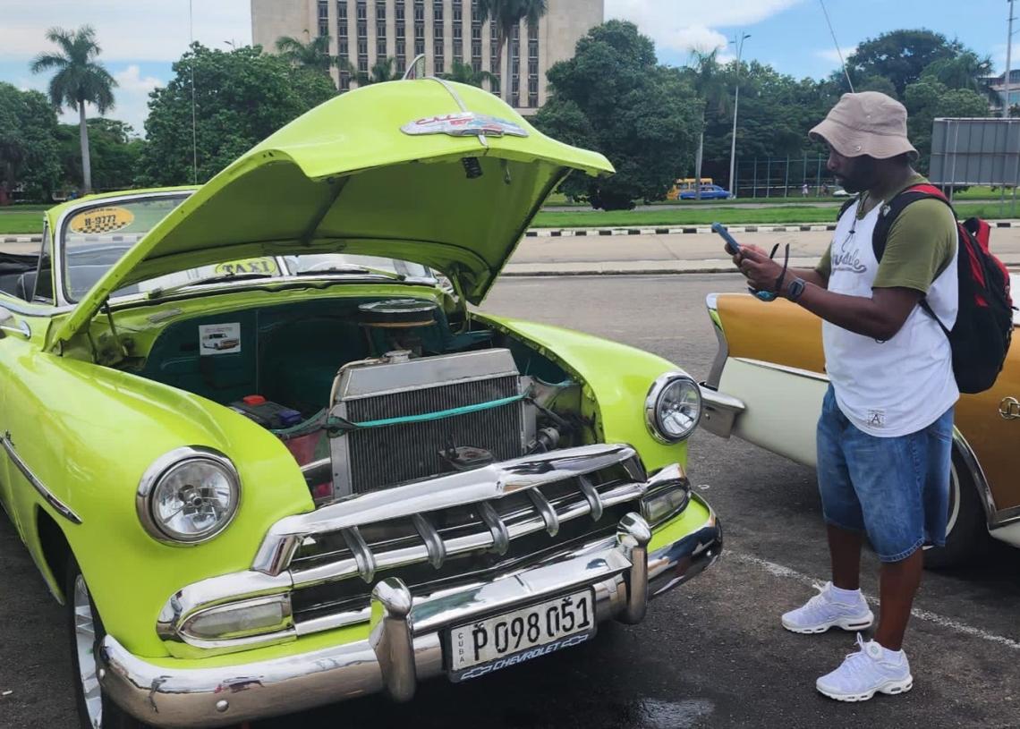 A man takes a picture of the engine in a green convertible in Havana's Revolutionary Plaza