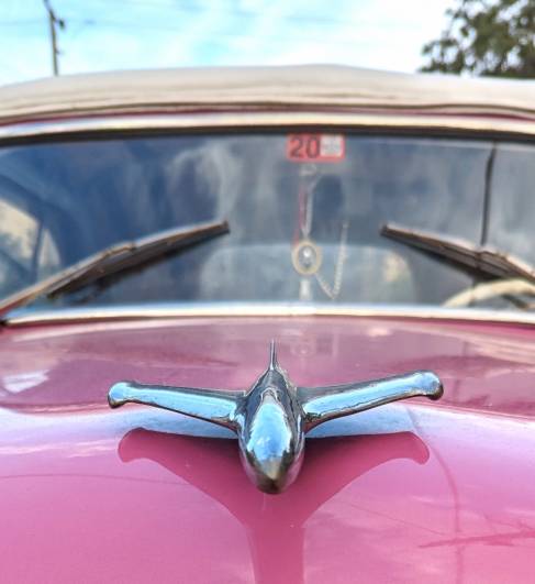 a pink classic car with a plan shaped hood ornament head on view a pink classic car with a plan shaped hood ornament head on view