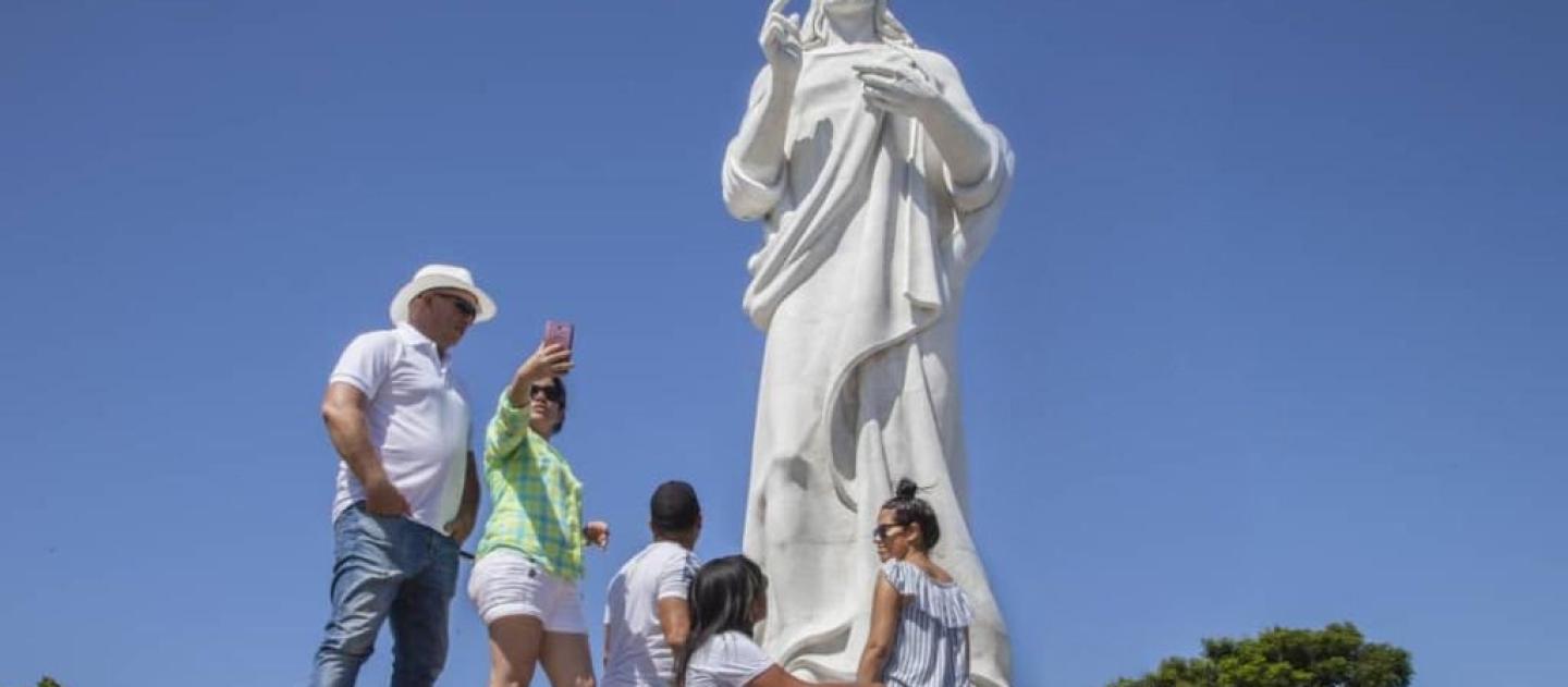 a group of people taking selfies in front of a tall white marble statue of Christ