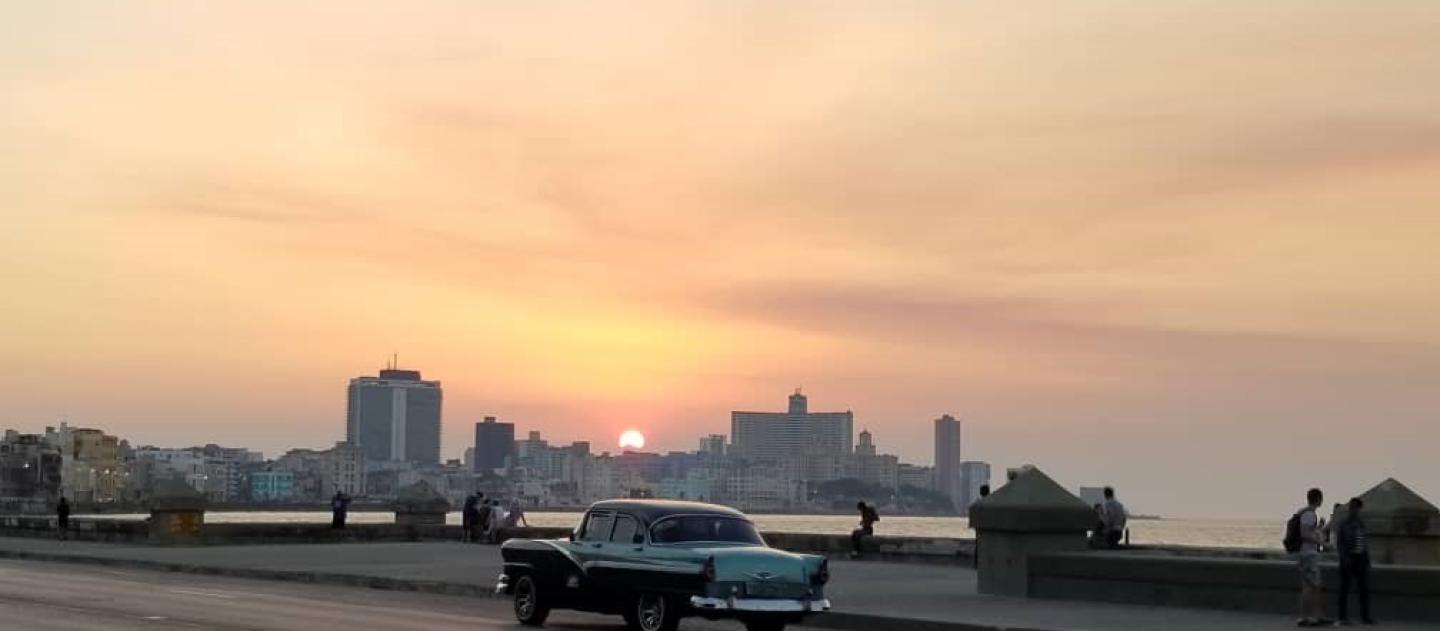 a classic car drives along a sea wall during sunset