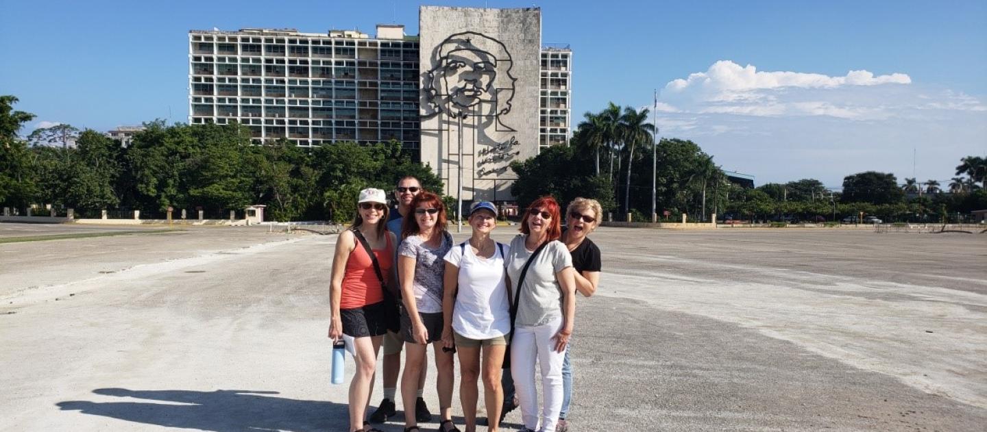 a group poses for a photo in front of a building decorated with a metal sculpture of Che Guevara