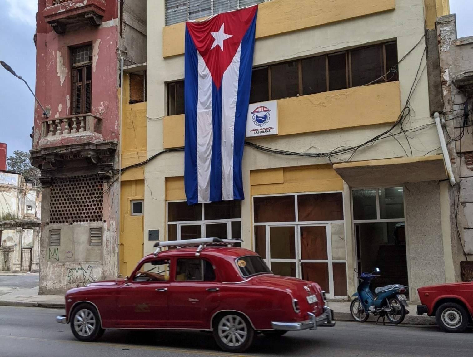 Red classic car in front of building adorned with Cuban flag Red classic car in front of building adorned with Cuban flag